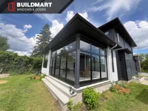 Modern black frame glass porch enclosure on a residential home exterior with large window panels and backyard view